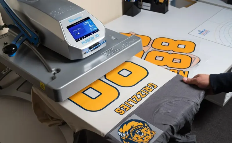 Een shirt wordt bedrukt onder de hittepers in het atelier